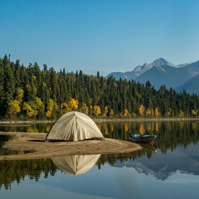 Tent on a sandy lakeshore below autumn forest and peaks