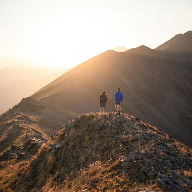 Two hikers on a grassy summit ridge at sunset